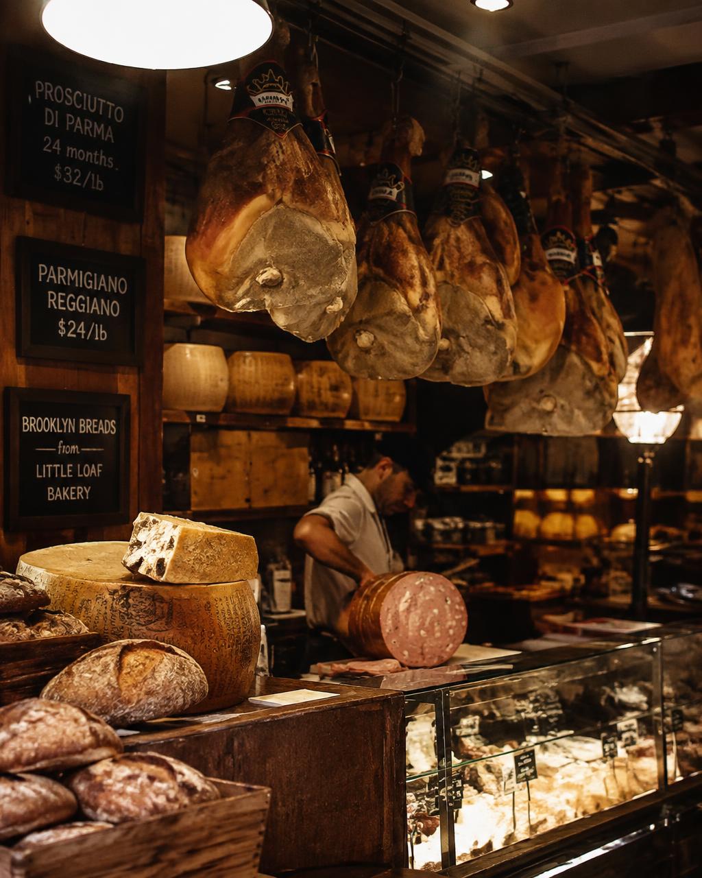 Italian deli counter with hanging prosciutto, parmigiano wheels and fresh loaves